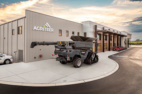 Agriteer headquarters building with company logo on metal facade and a precision farming autonomous dump vehicle parked on the curved driveway in front, under a dramatic sunrise sky